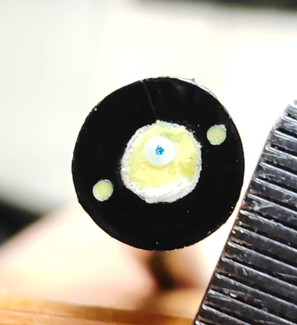 Cross-section of a fibre optic cable: black outer sheath, yellow fibrous packing, two small strength rods, and one blue-coated fibre at the centre